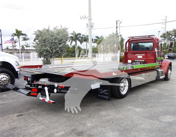 2022 Peterbilt 337 tow truck on a flatbed trailer, rear view showing flatbed and red cab, with some text stickers and rear lights.