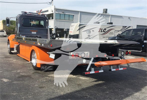 Truck bed with tow equipment on a purple Peterbilt 337; orange flatbed with rear loading ramps and TLC branding visible.