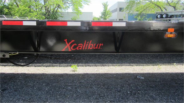 Flatbed trailer side showing Xcalibur logo in red on black steel frame.