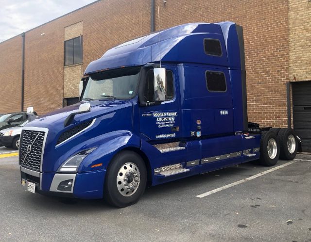 Volvo VNL64T860 truck in blue, side view showing sleeper cab, chrome steps, dual rear axles, logo text reading VNL and Volvo on grille, 6-wheel drive, business graphics on door.