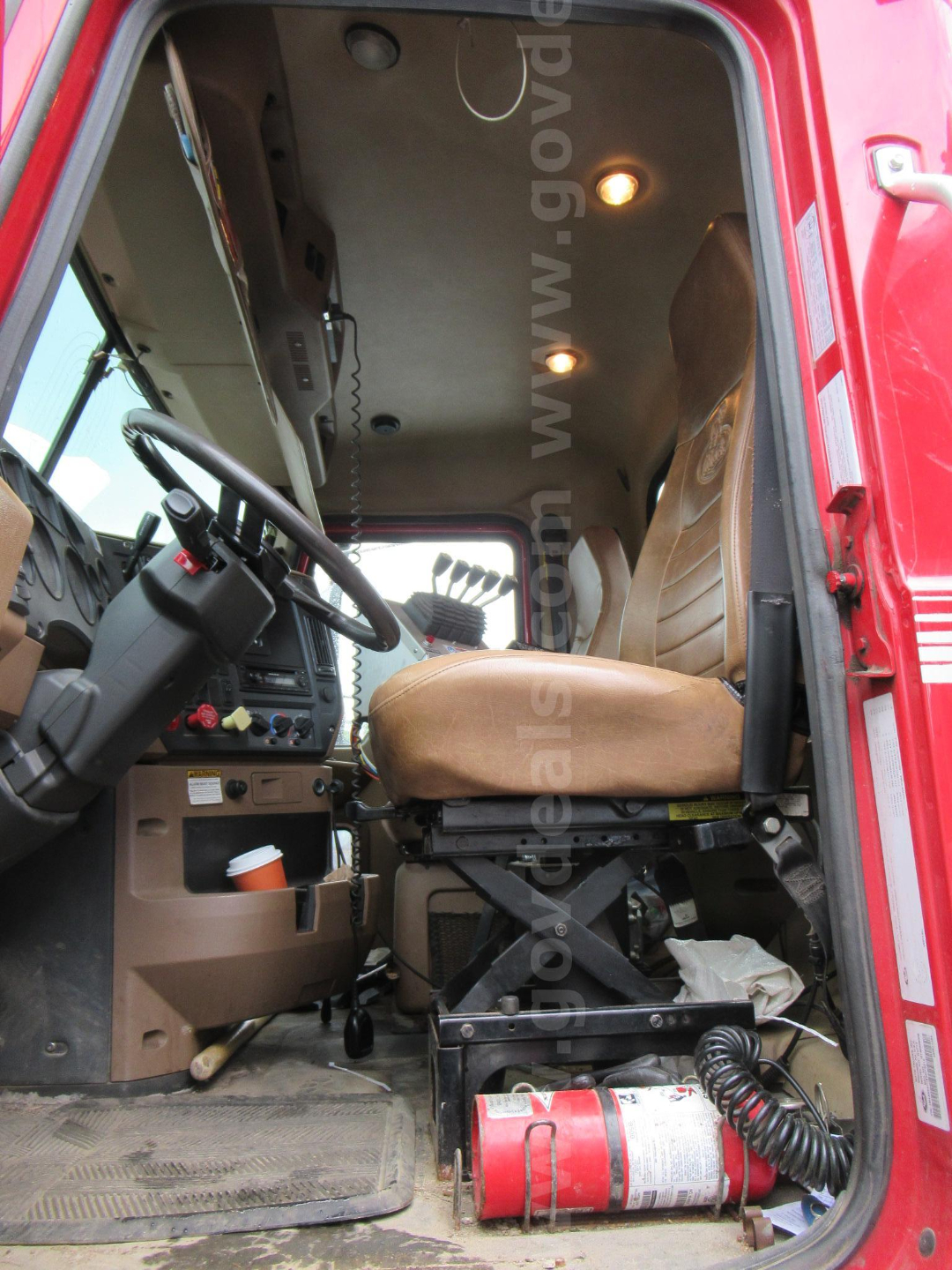 Cab interior of a red 2014 Mack GU713 truck showing steering wheel, dashboard, beige seat, fire extinguisher, and overhead lights.