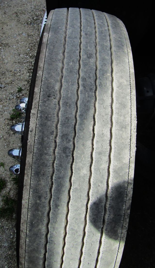 Truck tire tread close-up on a Kenworth T680 cab and chassis, showing long-worn tread grooves and sidewall of the tire.