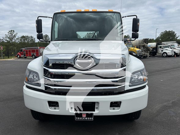 Front view of a white Hino L6 cab and chassis truck with chrome grille, Hino emblem, and bumper; orange clearance lights on roof; large side mirrors.