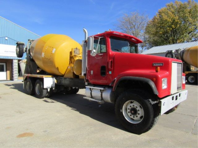 Concrete mixer truck with red cab and yellow drum, parked outdoors.