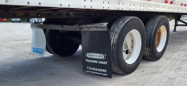 Trailer undercarriage showing dual rear axles, mud flaps with Freightliner Treasure Coast branding, and Vanguard mud flap logo.