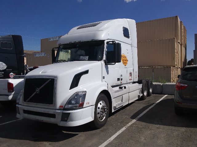Volvo 670 conventional sleeper truck in white, side view, with stacked shipping containers in background.