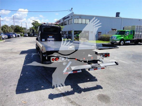 Tow truck bed with rear ramp and dual taillights, International MV chassis, rear view in a dealership lot.