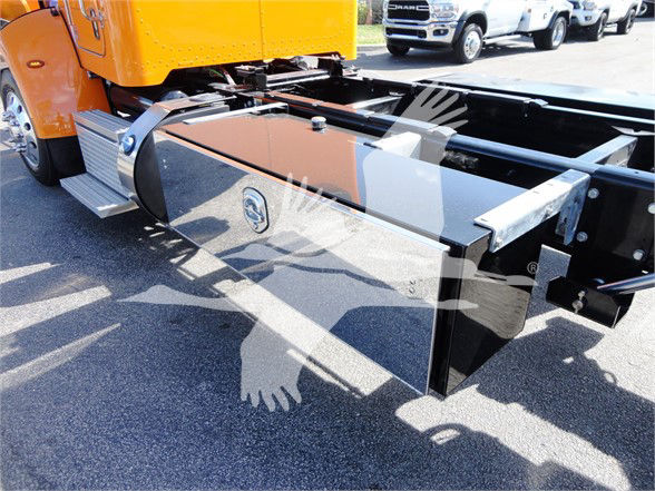 Truck chassis with glossy black side tank and orange cab visible, side tank showing chrome cap and metal steps with reflection on pavement.