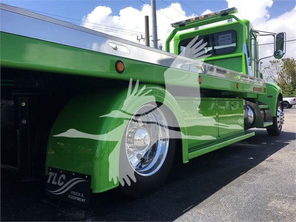Green Peterbilt 337 tow truck side view showing long flatbed and chrome wheel, stock number J52310, new unit.