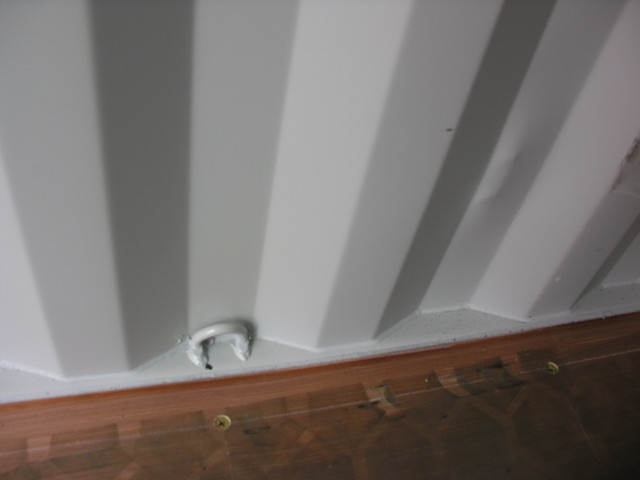 Container trailer side with vertical rib paneling and a small circular crank/dowel near the bottom edge over a wooden floor.
