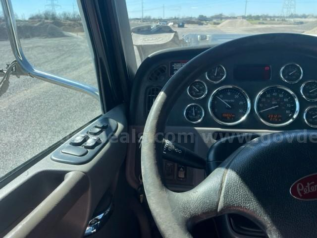 Peterbilt dashboard and steering wheel with multiple gauges in view, truck window and door controls visible.