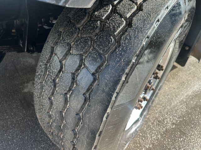Truck tire and wheel well showing heavy tread with some dirt; part of front axle visible.