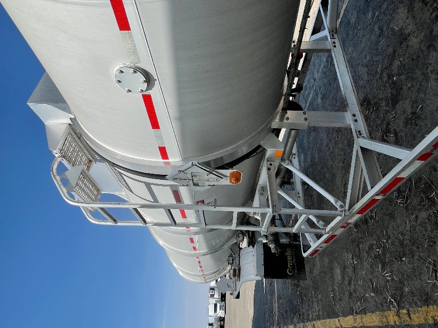 Aircraft-style trailer tank with ladder and platform, cylindrical tanker with red reflective stripe, parked in lot.