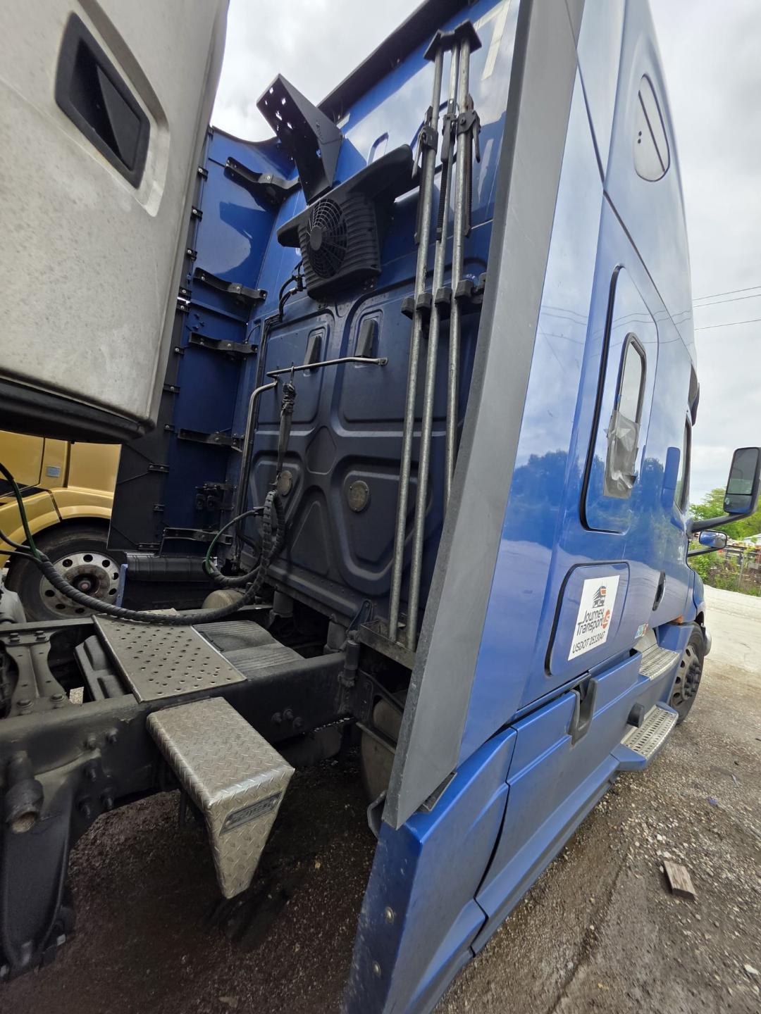 Freightliner Cascadia truck sleeper cab interior rear side with steps and hoses, blue exterior, metal steps, and wiring visible.