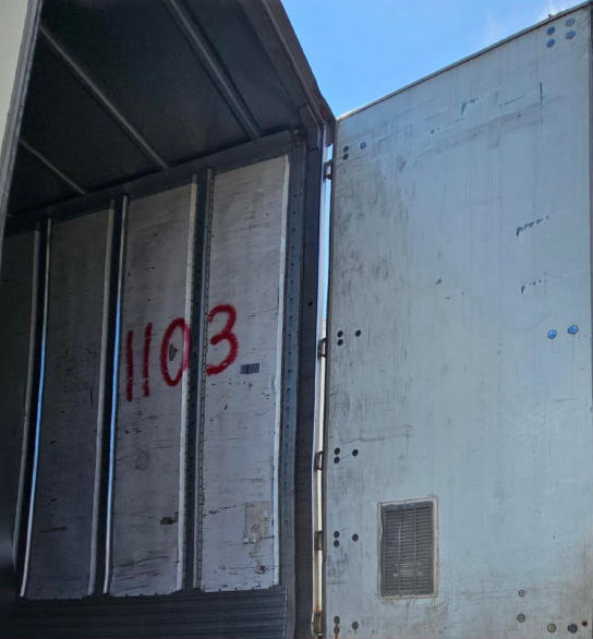 Trailer interior with open side door showing utility trailer walls and stair-step ribs; large red ‘1103’ marking visible.