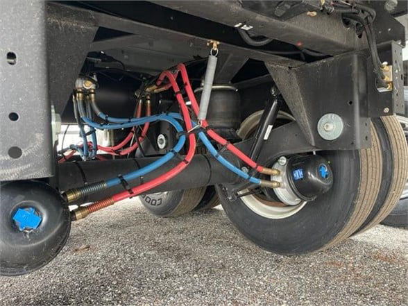 Underbelly of CIMC reefer trailer showing blue and red refrigerant lines, compressor, hoses, and wheel assembly.