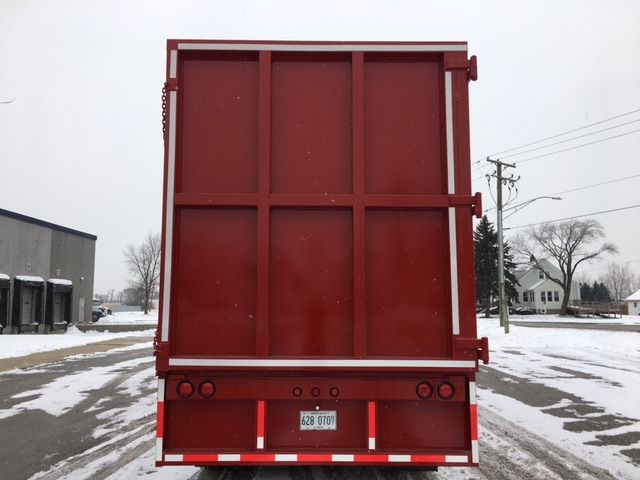 Rear view of a red dump trailer with a metal gate, lights, and license plate visible.