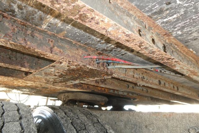 Rusty trailer frame with exposed metal beams and wheels visible underneath, showing corrosion and support structure.