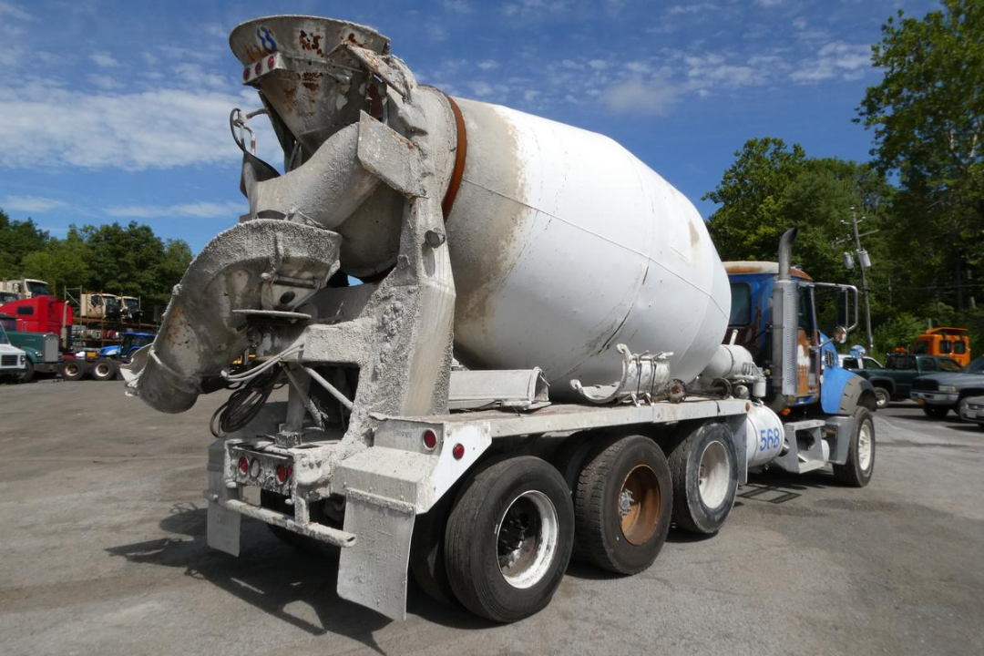 Mixer truck with large cement mixer drum at rear, rear view showing multiple axles and weathered white paint.