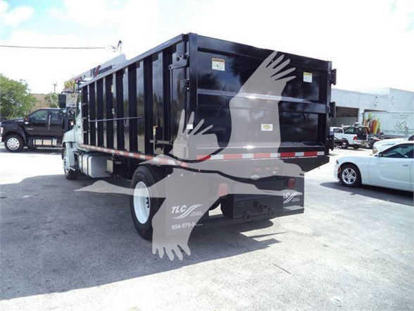 Dump truck with a black bed and white cab showing a large dump hopper from rear left side.