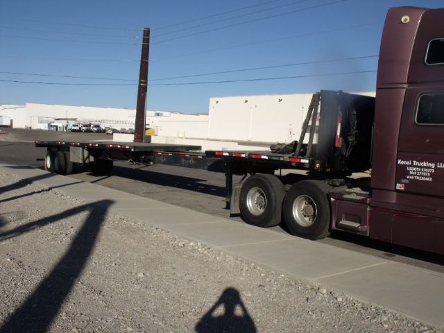 Flatbed tractor-trailer with extended Fontaine trailer in 48 to 80 foot expandable configuration, parked on a paved lot; visible are the long flat deck, rear axles, and a maroon truck cab.