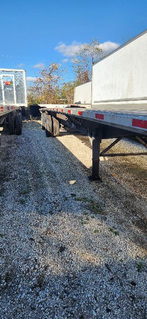 Trailer hitch and frame of a utility combo flatbed trailer with gravel ground, other trailers in background.