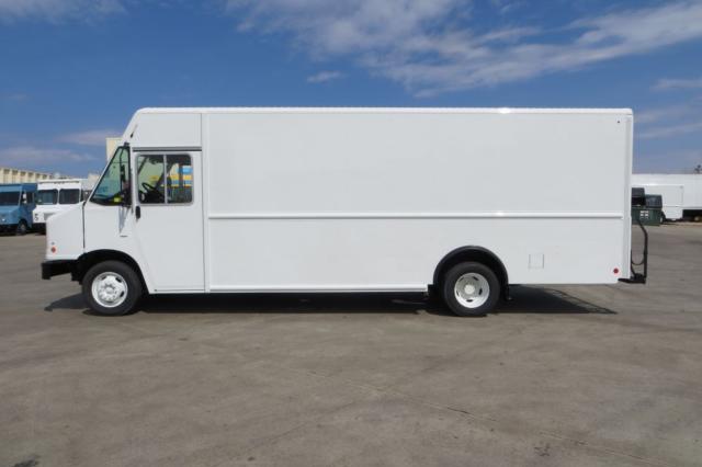 Boxy white 2015 Ford F59 step van side view showing cargo box and cab, with blue sky and other vehicles in the background.