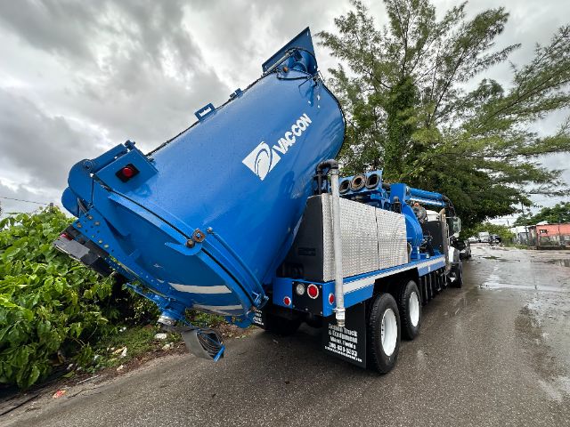 Clear view of a blue Mack GU713 vacuum truck with large tilted tank and multiple axles, rear view showing hoses and platforms.