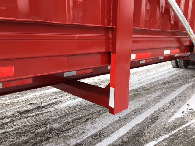 Red trailer side with lower support beam in a snowy lot and reflective tape along the edge.