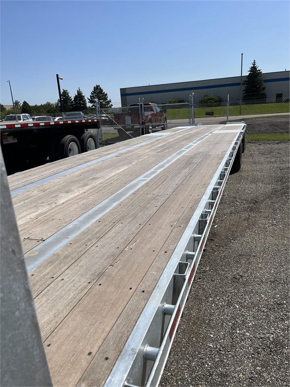 Manac steel stepdeck trailer with wooden deck and steel framework, parked in lot.