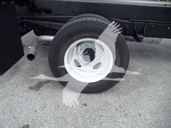 Truck wheel and undercarriage showing rear tire with white steel rim and exhaust pipe