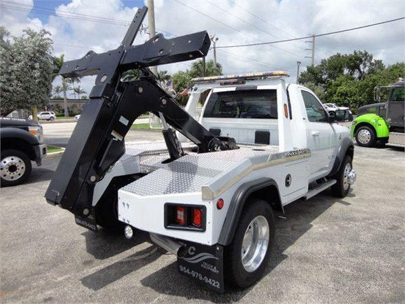 Front-left view of a white 2024 Ram 4500 SLT tow truck with a large black hydraulic hook at the rear, in a parking lot.