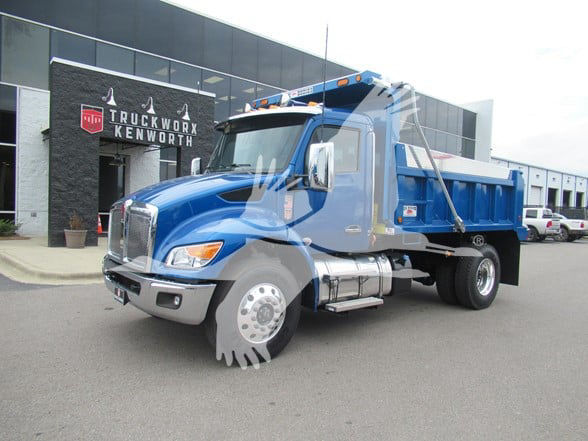 Kenworth T380 dump truck in blue with silver front, parked outside dealership, front three-quarter view.