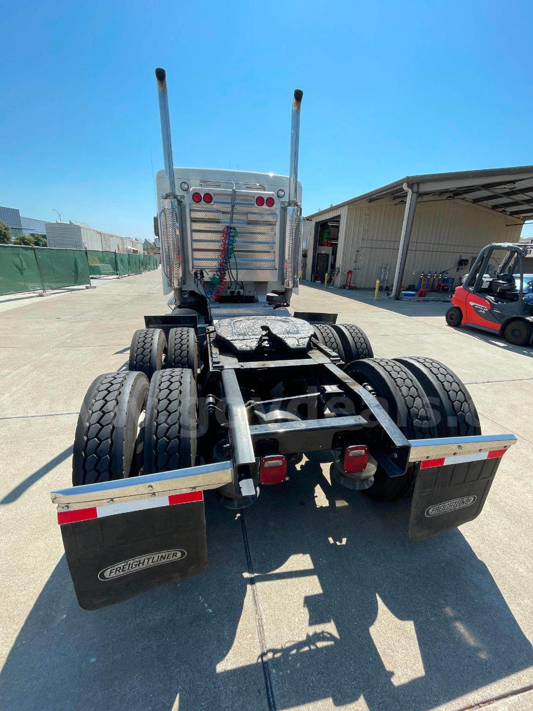 Rear view of a Freightliner Columbia 120 tractor chassis showing dual rear axles, fuel tanks, and exhaust stacks.