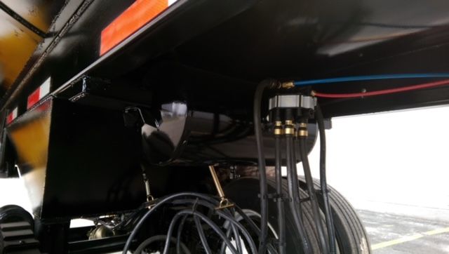 Underbelly of trailer showing hydraulic hoses and fittings with metal components.