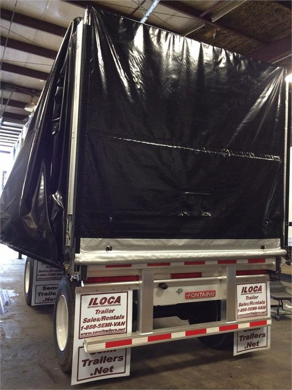 Rear view of a Fontaine trailer with a black tarp system cover, white metal frame, and red-and-white reflective safety markings.