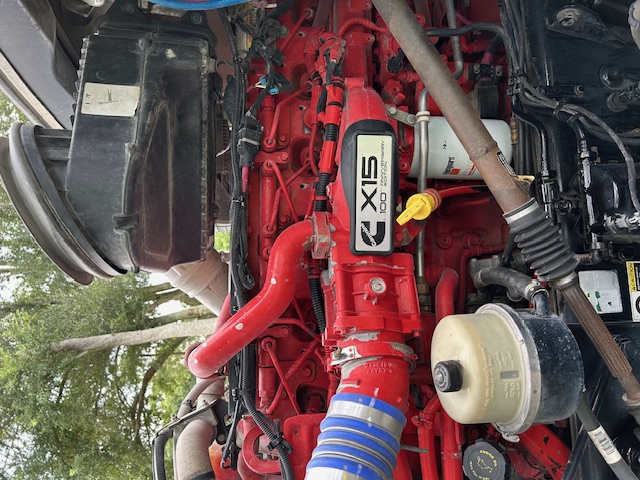 Picture of a red Caterpillar/ Cummins engine panel with X15 badge visible on engine cover and surrounding hoses and components in Peterbilt truck engine bay.