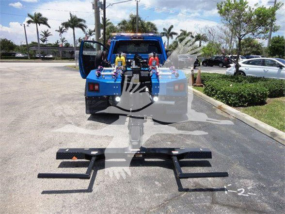 Blue Ram pickup in tow configuration with a loader and rear equipment visible; hydraulic hoses and metal mount arms laid out on the ground.