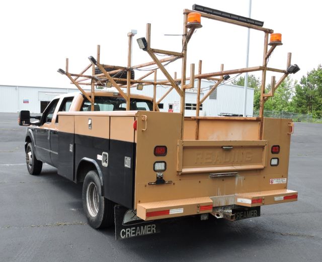 Ford F-350 utility truck with wooden ladder racks in tan and black colors, rear tailgate, and Creeamer mud flaps visible.