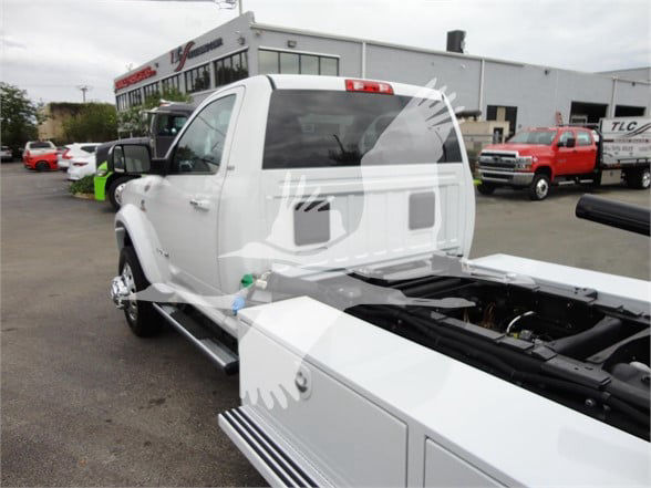white Ram 5500 HD tow truck chassis with cab, rear view showing bed, stickers blurred, dealership lot in background.