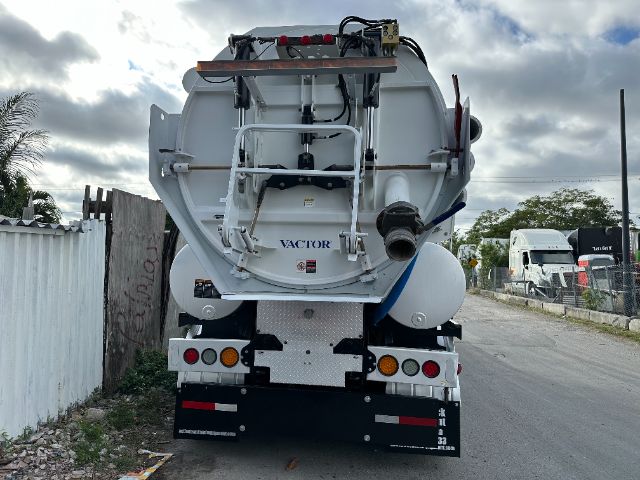 Rear view of a white Freightliner M2 vacuum truck with equipment mounted, showing hoses, valves, and a Vactor badge on the tank.