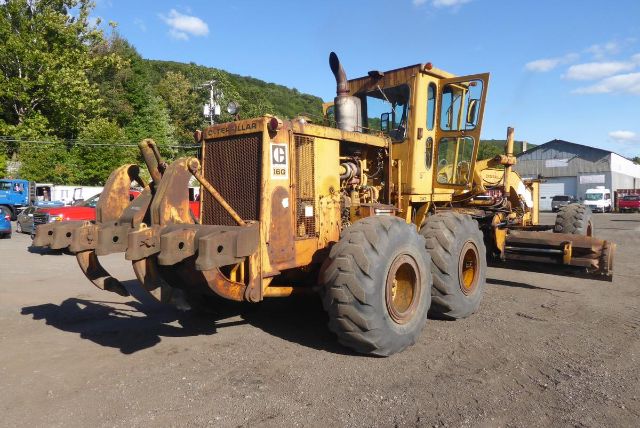 Caterpillar 16G motor grader with yellow body and large off-road tires, front view showing hydraulic arms and blade attachment area.