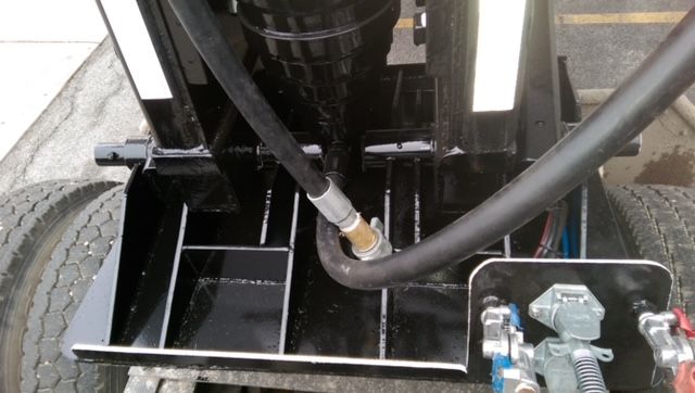 Dump trailer undercarriage showing hydraulic hose attached to a valve block and circular wheel rims.