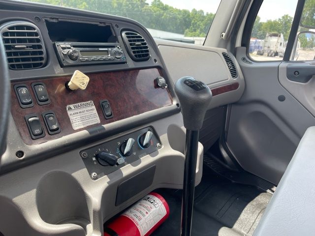 Dashboard of a Freightliner M2 cab showing steering column, radio, climate controls, and a fire extinguisher at the footwell.