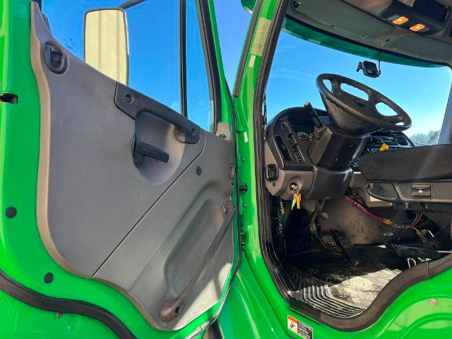 Truck cab interior of a 2016 Freightliner M2 106 with bright green exterior, black steering wheel, dashboard, and open door showing the entry area.