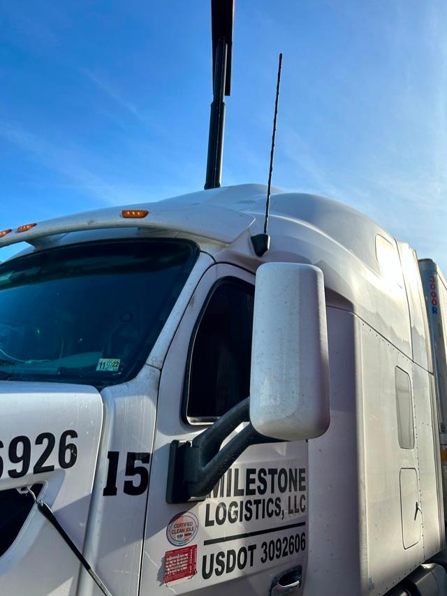 Truck cab exterior showing Peterbilt logo area with large white sleeper, antenna, side mirror, and company graphics including USDOT and logistics labeling.