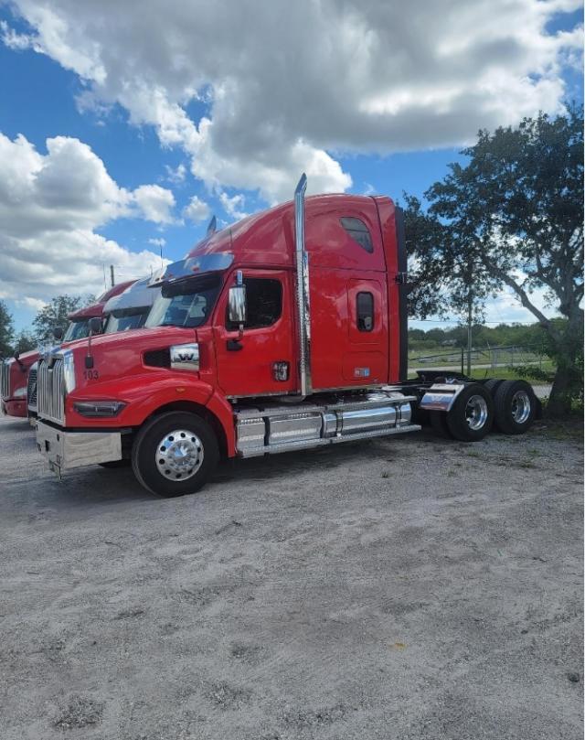Red 2023 Western Star 4900 conventional sleeper truck from side view showing chrome fuel tanks and triple rear bogie undercarriage.