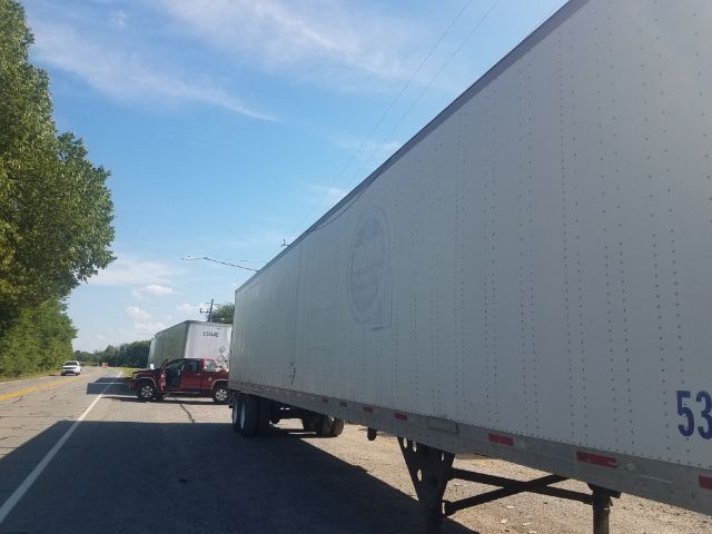 A white utility trailer with side branding and a blue sky, long trailer on a road with other trailers in the background.