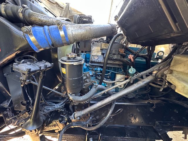 Truck engine bay showing air intake hose, oil filter, and blue-painted engine block with various hoses and wiring.