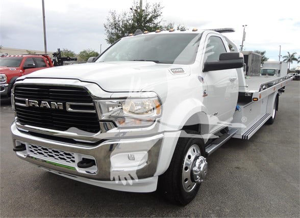 Ram 5500 HD tow truck with large chrome grille, RAM lettering on grille, white cab, flatbed tow truck body, headlights visible.